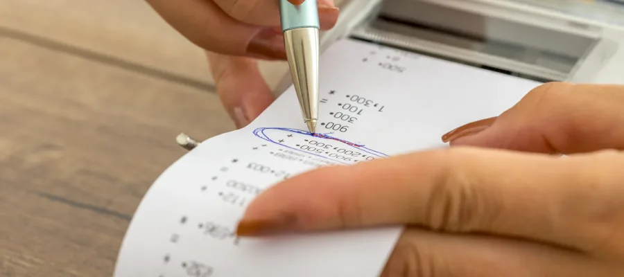 Tax and accounting business concept - closeup of female hands working with adding machine and printout circling important figures wit a pen.
